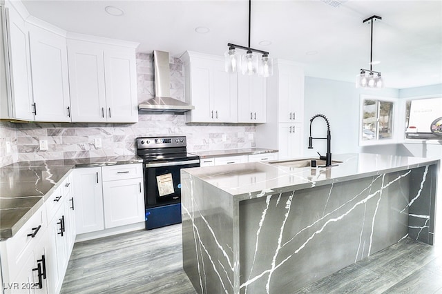 kitchen featuring a kitchen island with sink, electric range, a sink, wall chimney range hood, and decorative backsplash