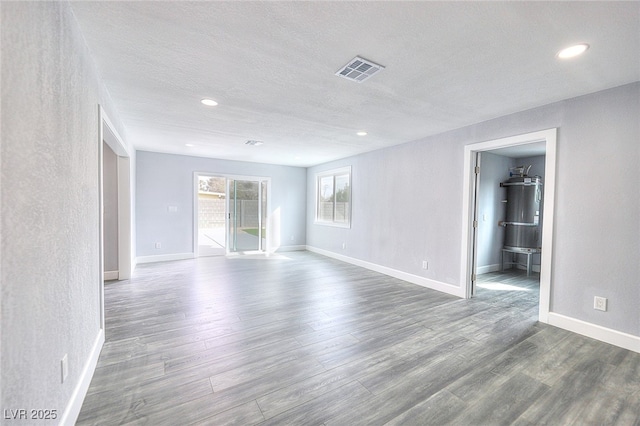 spare room featuring a textured ceiling, wood finished floors, visible vents, baseboards, and secured water heater