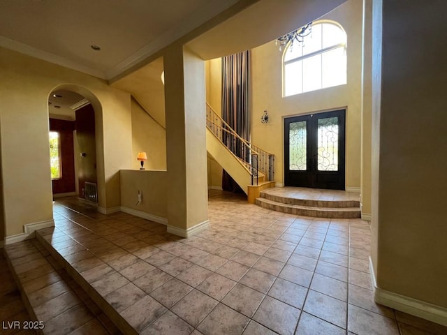 entrance foyer with french doors, a towering ceiling, ornamental molding, and light tile patterned floors