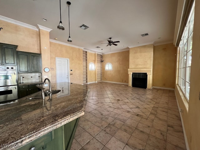 kitchen featuring green cabinetry, ornamental molding, a tiled fireplace, and double oven