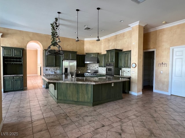 kitchen featuring dark stone countertops, hanging light fixtures, a large island with sink, stainless steel appliances, and crown molding