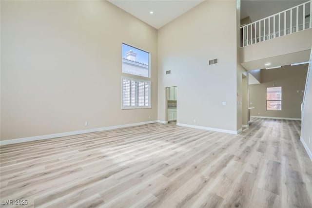 unfurnished living room featuring visible vents, light wood-style flooring, baseboards, and a towering ceiling