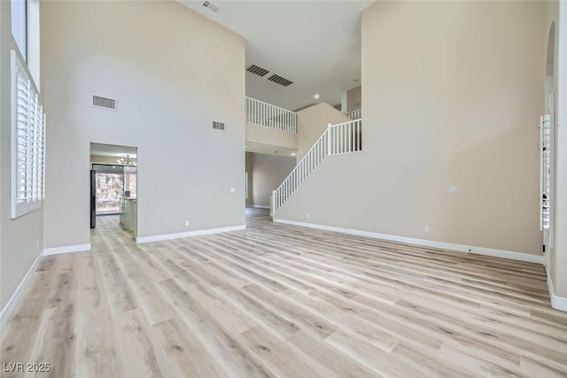 unfurnished living room with a towering ceiling and light hardwood / wood-style floors