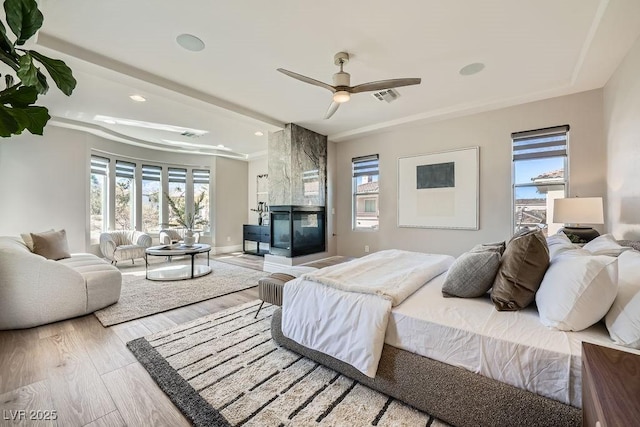 bedroom featuring multiple windows, a multi sided fireplace, ceiling fan, and light hardwood / wood-style flooring