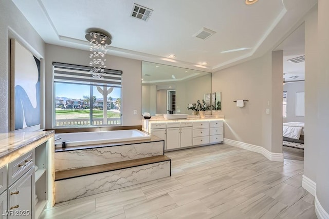 bathroom with a relaxing tiled tub, vanity, and a tray ceiling