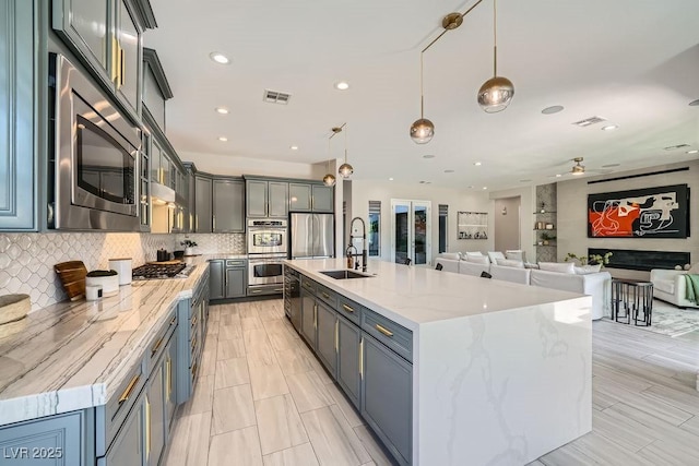 kitchen with tasteful backsplash, sink, hanging light fixtures, a kitchen island with sink, and stainless steel appliances