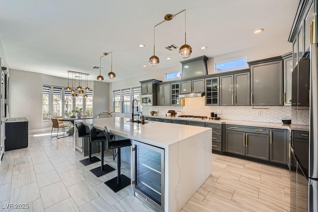 kitchen with appliances with stainless steel finishes, an island with sink, a kitchen bar, decorative light fixtures, and beverage cooler