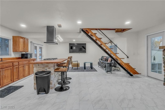 kitchen featuring a kitchen bar, island range hood, a kitchen island, decorative light fixtures, and stainless steel gas stovetop