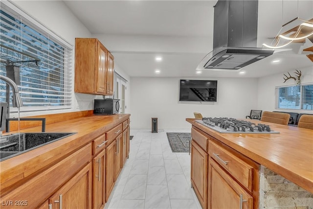 kitchen with sink, wooden counters, decorative light fixtures, island exhaust hood, and stainless steel gas stovetop