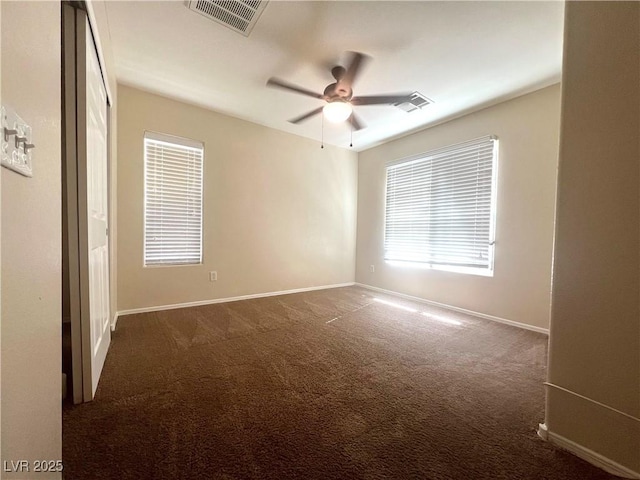 spare room featuring visible vents, dark carpet, baseboards, and ceiling fan