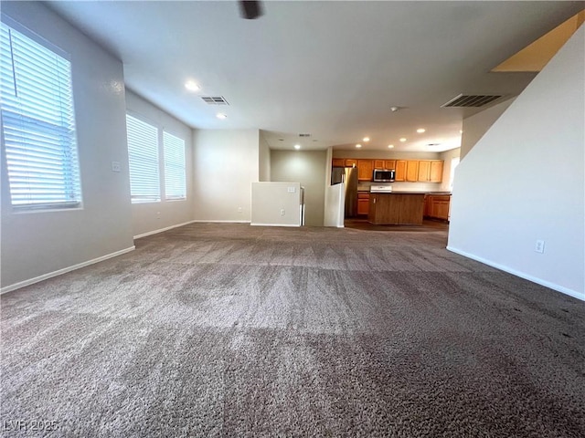 unfurnished living room with visible vents, dark carpet, and baseboards