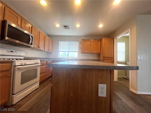 kitchen featuring dark wood-style floors, visible vents, white range with gas stovetop, and stainless steel microwave