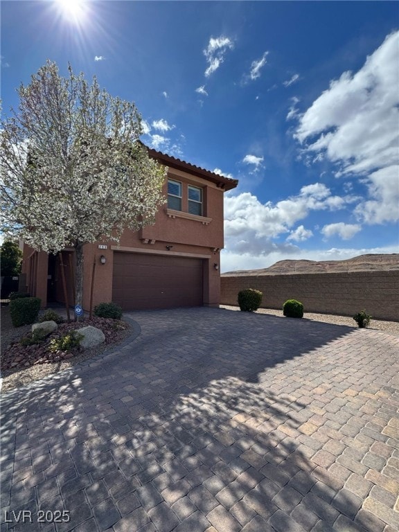 view of front facade with decorative driveway, a tile roof, an attached garage, and stucco siding