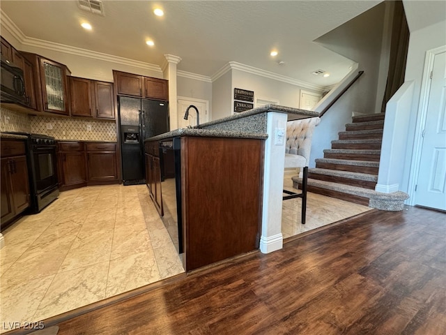 kitchen featuring a breakfast bar area, dark brown cabinetry, visible vents, decorative backsplash, and black appliances