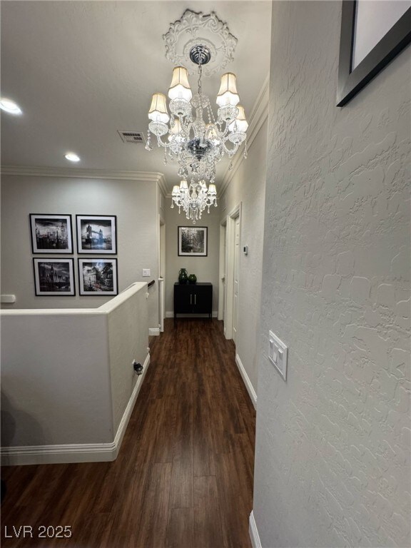 hallway with a textured wall, ornamental molding, and visible vents