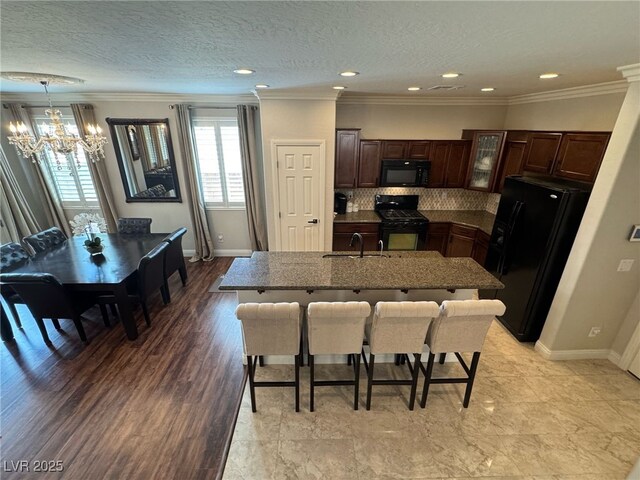 kitchen featuring a sink, a kitchen breakfast bar, decorative backsplash, black appliances, and crown molding