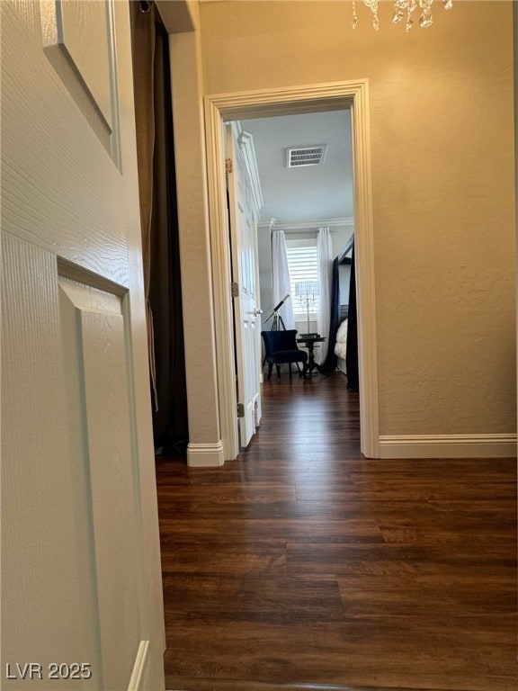 hallway with baseboards, visible vents, a textured wall, dark wood-style floors, and ornamental molding