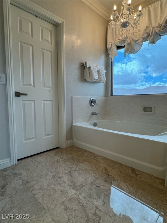 full bathroom featuring an inviting chandelier, baseboards, a garden tub, and crown molding