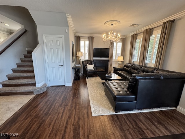 living room featuring dark wood-style flooring, visible vents, stairway, ornamental molding, and a glass covered fireplace