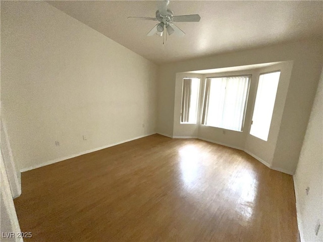 unfurnished room featuring ceiling fan, baseboards, vaulted ceiling, and wood finished floors