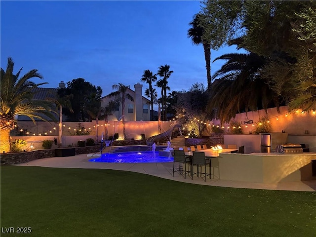 pool at dusk featuring pool water feature, area for grilling, a lawn, a bar, and a patio