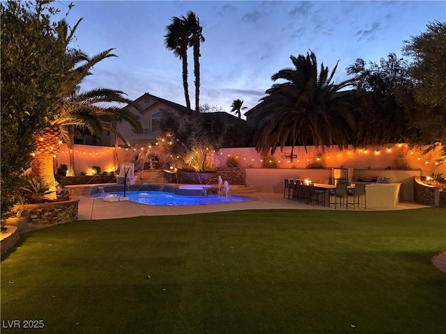 pool at dusk featuring exterior bar, area for grilling, pool water feature, a yard, and a patio area