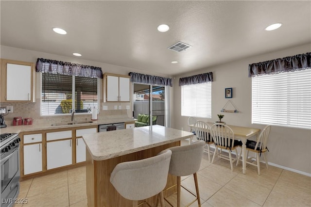 kitchen featuring sink, dishwasher, white cabinetry, a center island, and gas range