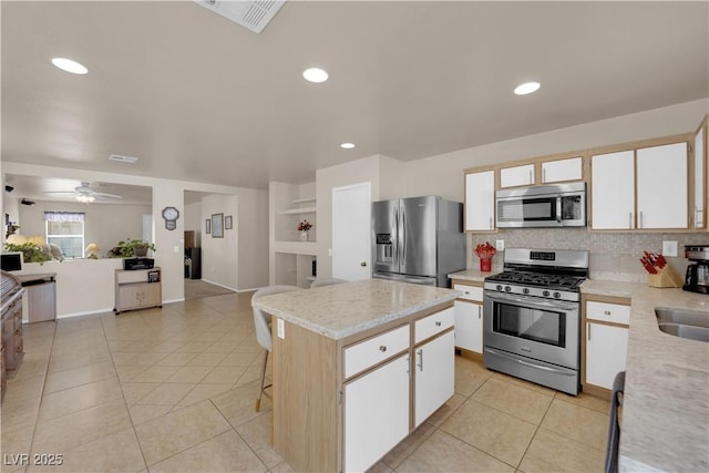 kitchen with stainless steel appliances, a kitchen island, light tile patterned floors, and white cabinets