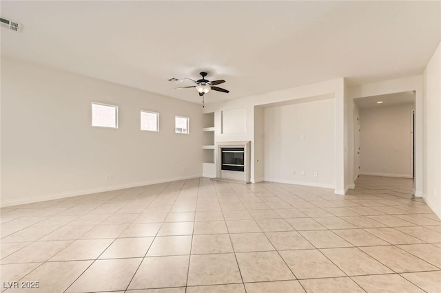 unfurnished living room with light tile patterned floors, visible vents, a ceiling fan, baseboards, and a glass covered fireplace