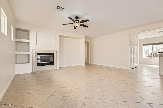 unfurnished living room featuring light tile patterned floors, visible vents, a ceiling fan, a glass covered fireplace, and baseboards