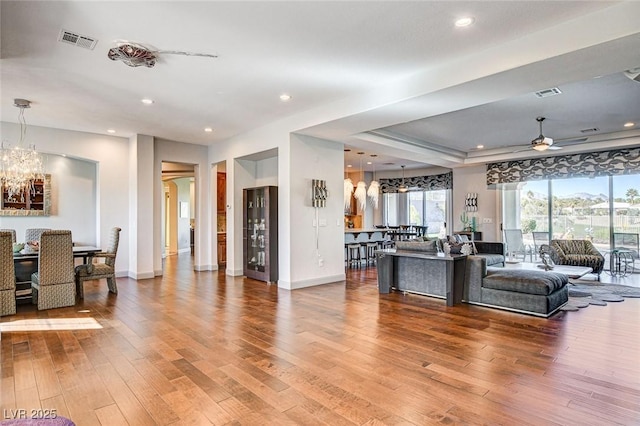 living room with hardwood / wood-style flooring, a raised ceiling, and ceiling fan with notable chandelier