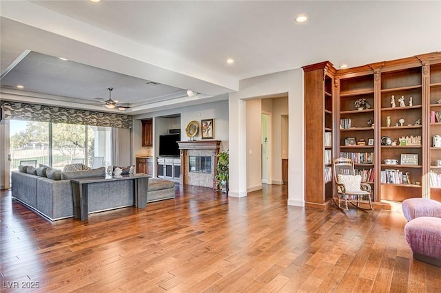 living room with ceiling fan, a tiled fireplace, hardwood / wood-style floors, and a raised ceiling