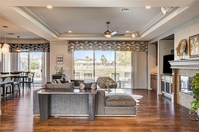 living room featuring a raised ceiling, a tile fireplace, dark wood-type flooring, and ceiling fan