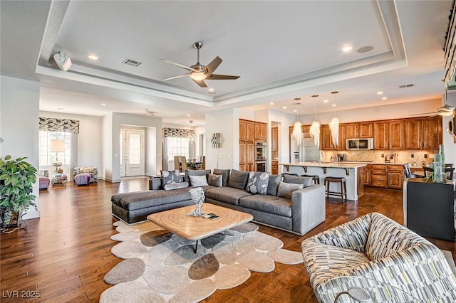 living room with ceiling fan, plenty of natural light, and a raised ceiling