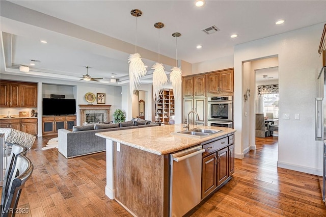 kitchen with dark wood-type flooring, appliances with stainless steel finishes, sink, and a kitchen island with sink