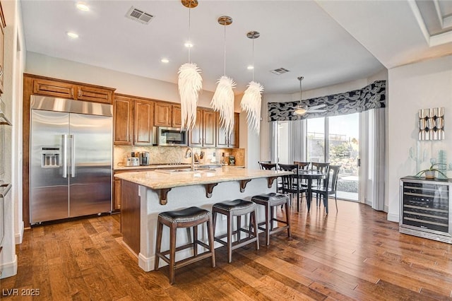 kitchen featuring pendant lighting, tasteful backsplash, light stone counters, stainless steel appliances, and a center island with sink