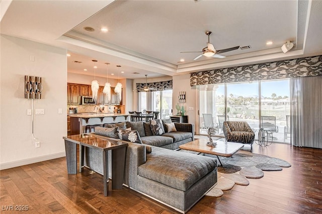 living room with a raised ceiling, dark hardwood / wood-style floors, and ceiling fan