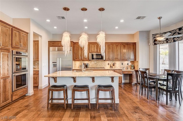 kitchen with light stone countertops, decorative light fixtures, stainless steel appliances, and a center island with sink