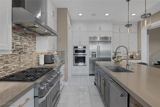 kitchen with white cabinets, a sink, wall chimney range hood, and high quality appliances