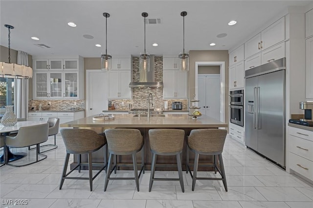 kitchen with wall chimney range hood, visible vents, stainless steel appliances, and a kitchen breakfast bar