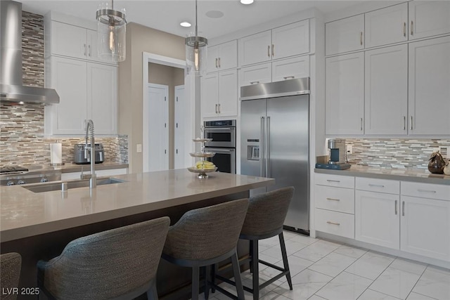 kitchen featuring appliances with stainless steel finishes, white cabinets, wall chimney range hood, and a kitchen bar