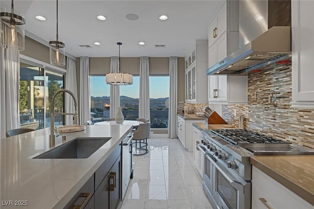 kitchen featuring visible vents, wall chimney range hood, a sink, and appliances with stainless steel finishes