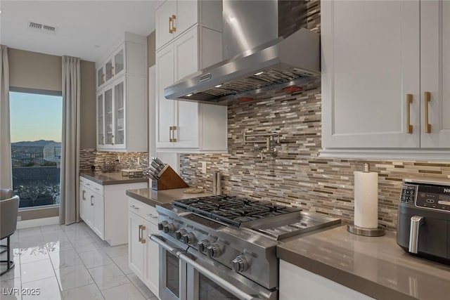 kitchen with range with two ovens, dark countertops, visible vents, white cabinetry, and wall chimney exhaust hood