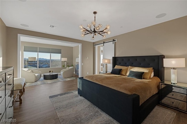 bedroom featuring a chandelier, wood finished floors, visible vents, and a barn door