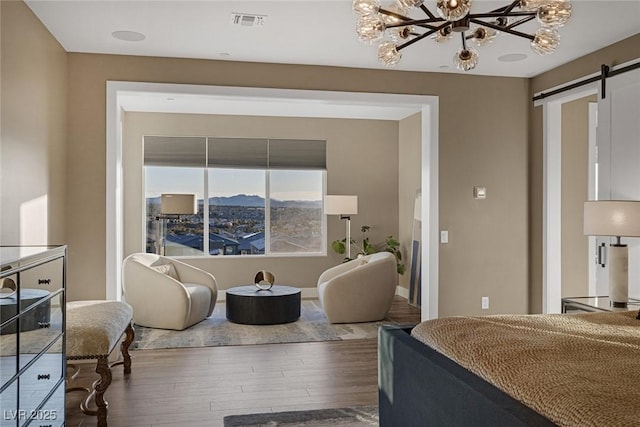 bedroom featuring a barn door, visible vents, wood finished floors, an inviting chandelier, and a mountain view