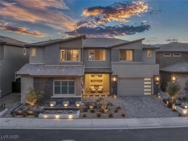 contemporary house featuring stone siding, decorative driveway, an attached garage, and stucco siding