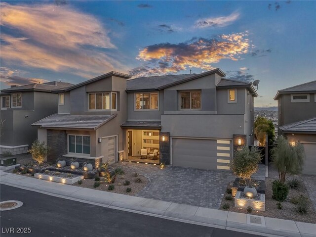 view of front of home featuring stone siding, decorative driveway, an attached garage, and stucco siding