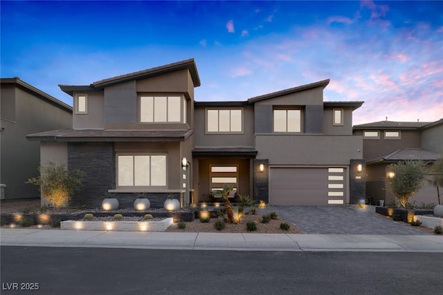 contemporary house with a garage, stone siding, decorative driveway, and stucco siding