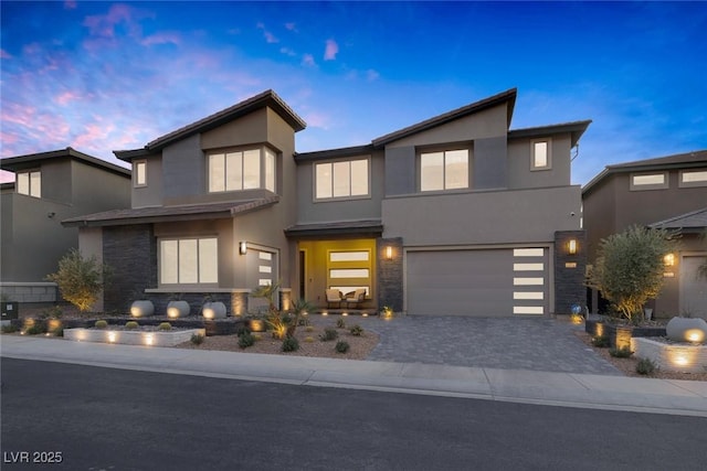 contemporary home with a garage, decorative driveway, stone siding, and stucco siding