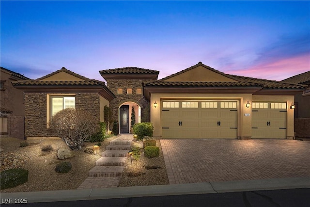 mediterranean / spanish-style house with a garage, stone siding, a tiled roof, decorative driveway, and stucco siding